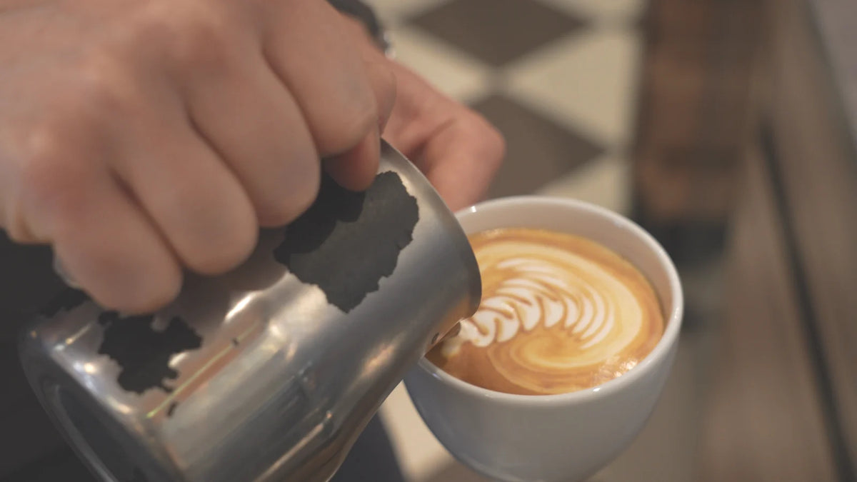 Milch wird für die Latte Art in eine Cappuccinotasse gegossen