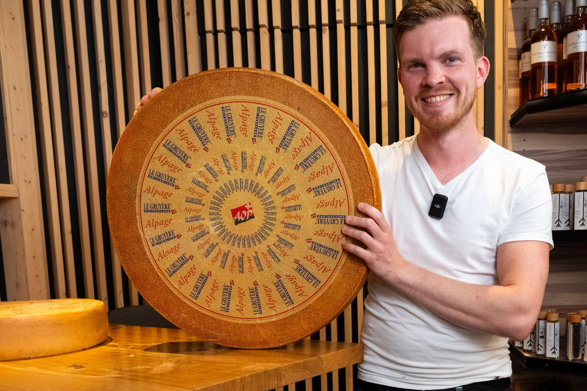 Mitarbeiter der Fromagerie Geiß hält einen ganzen Laib Le Gruyère Alpage AOP