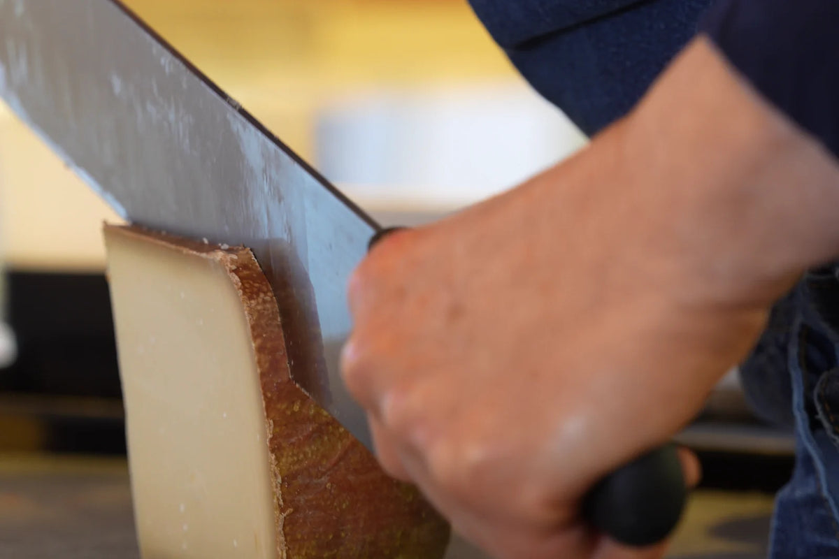 Ein Stück Hartkäse wird mit dem Käsemesser abgeteilt