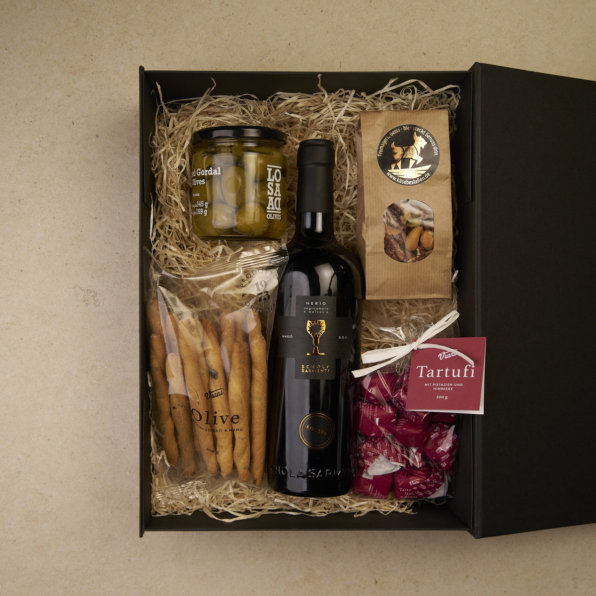 Geschenkbox Kaminabend, geöffnet: Nerìo Rotwein, Gordal-Oliven, Grissini, Tartufi und Nussmix auf Holzwolle