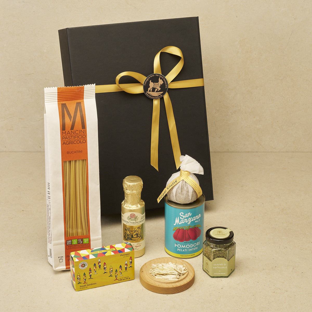 Geschenkbox Kochabend: Bucatini, Olivenöl, Belper Knolle, San Marzano, Origano und Sardinen vor der schwarzen Magnetbox