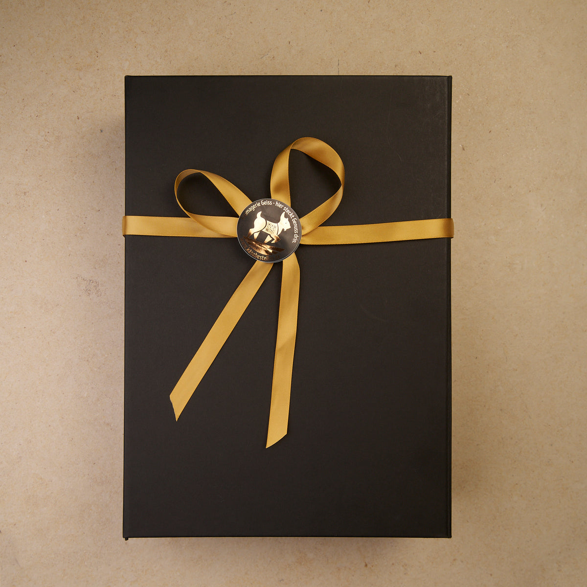 Geschlossene schwarze Geschenkbox mit Goldband und Siegel der Fromagerie Geiß