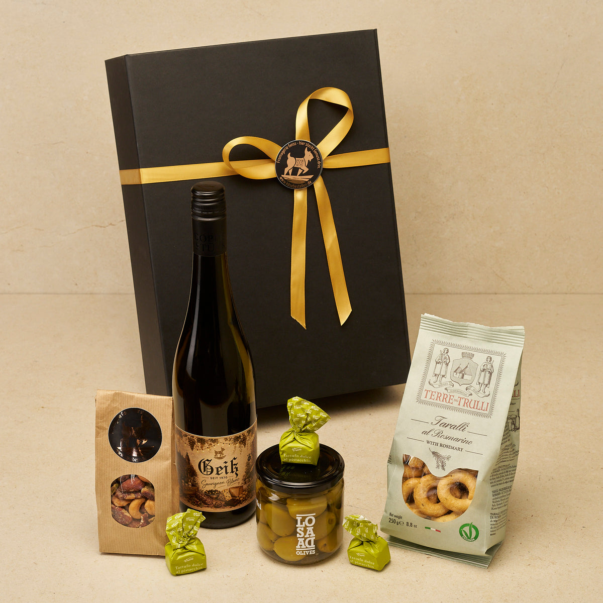Geschenkbox Weingruß groß: Geiß Sauvignon Blanc, Nussmix, Tartufi Pistacchio, Gordal-Oliven und Taralli vor der schwarzen Magnetbox