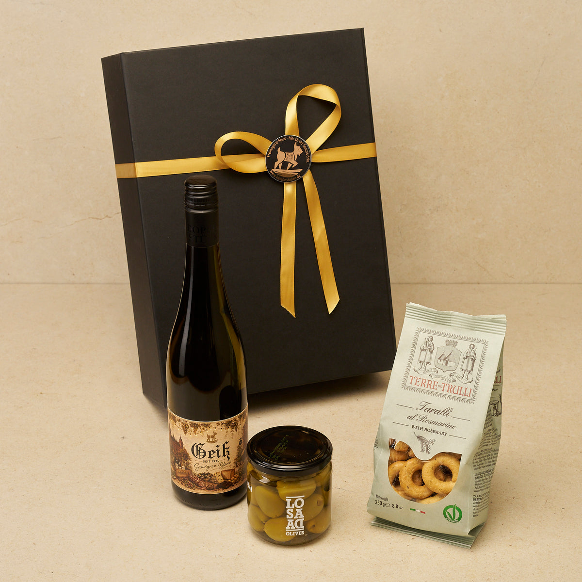 Geschenkbox Weingruß klein: Geiß Sauvignon Blanc, Gordal-Oliven und Taralli vor der schwarzen Magnetbox
