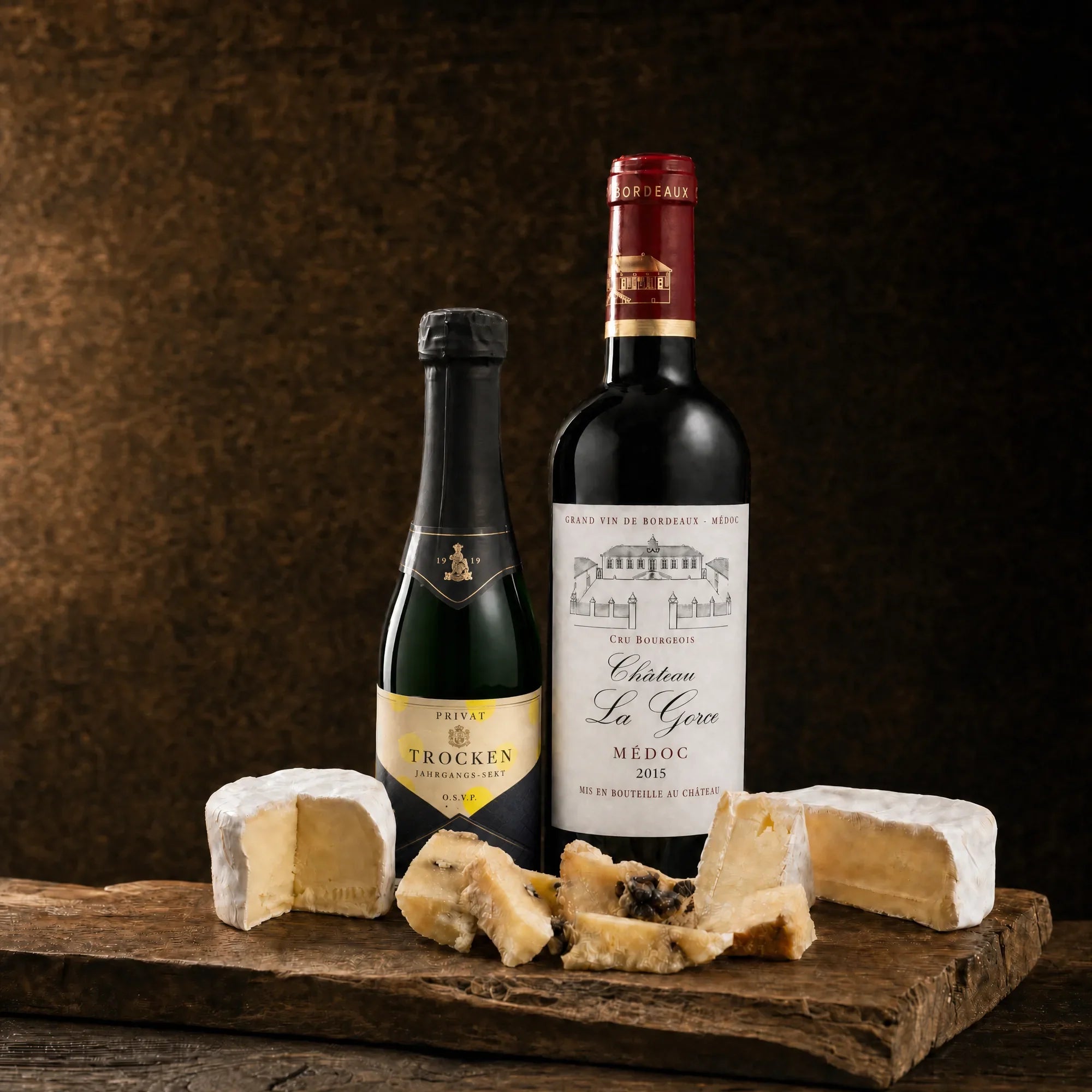 Tasting-Box Duo Rubis: Jahrgangs-Sekt-Piccolo und Rotwein Château La Gorce Médoc mit Käseauswahl auf rustikalem Holzbrett