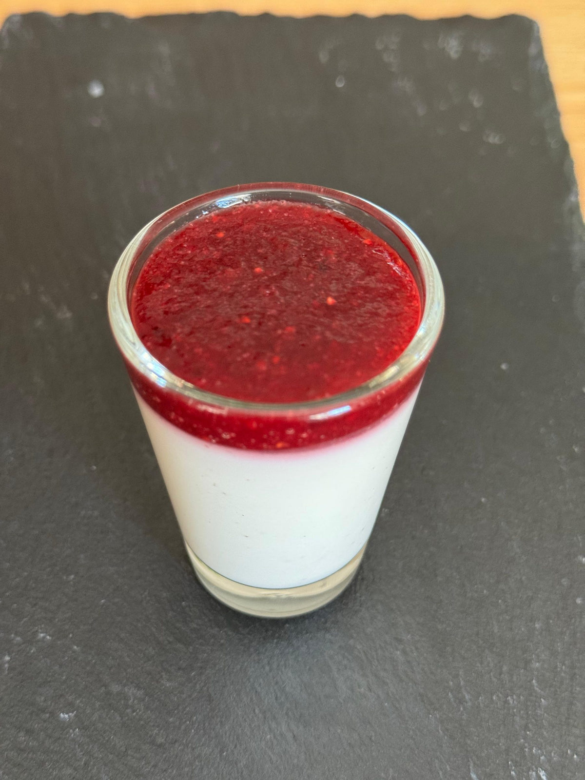 Panna cotta mit rotem Fruchtspiegel im Glas auf einer Schieferplatte