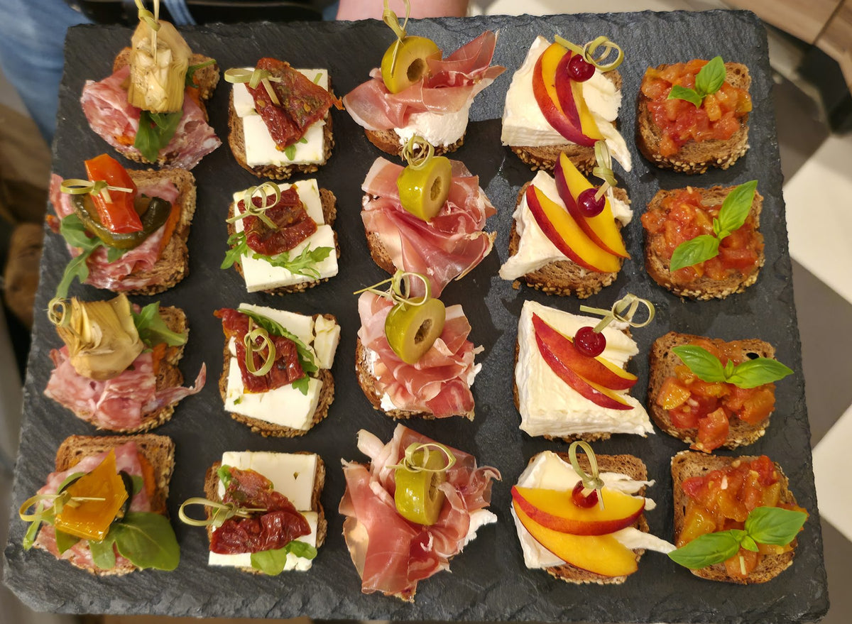 Belegte Canapés mit Salami, Käse, Schinken, Pfirsich und Tomate auf einer Schieferplatte