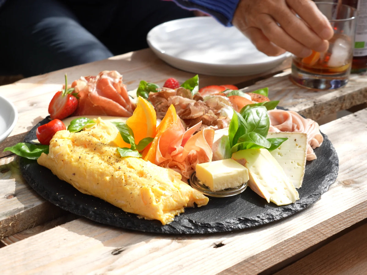 Frühstücksteller mit Omelett, Schinken, Käse und Obst auf einer Schieferplatte