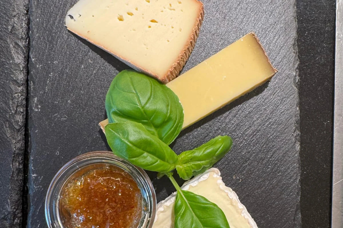 Detail einer Käseplatte mit Hartkäse, Weichkäse, Feigensenf und Basilikum