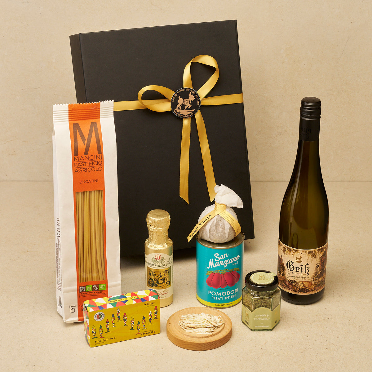 Geschenkbox Kochabend mit Wein: Bucatini, Olivenöl, Belper Knolle, San Marzano, Origano, Sardinen und Geiß Sauvignon Blanc vor der schwarzen Magnetbox