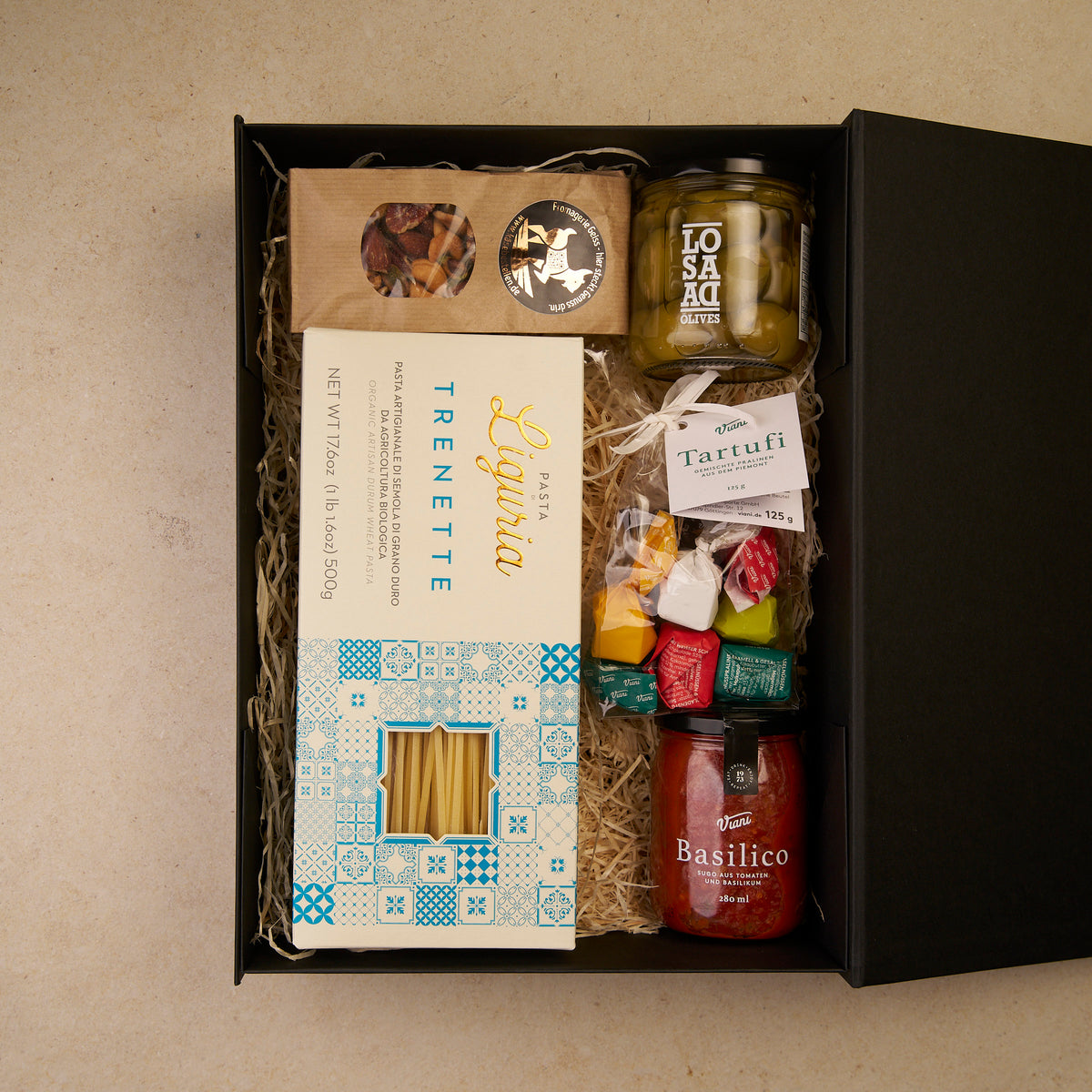 Geschenkbox Pastaliebe, geöffnet: Trenette, Sugo Basilico, Tartufi, Gordal-Oliven und Nussmix auf Holzwolle