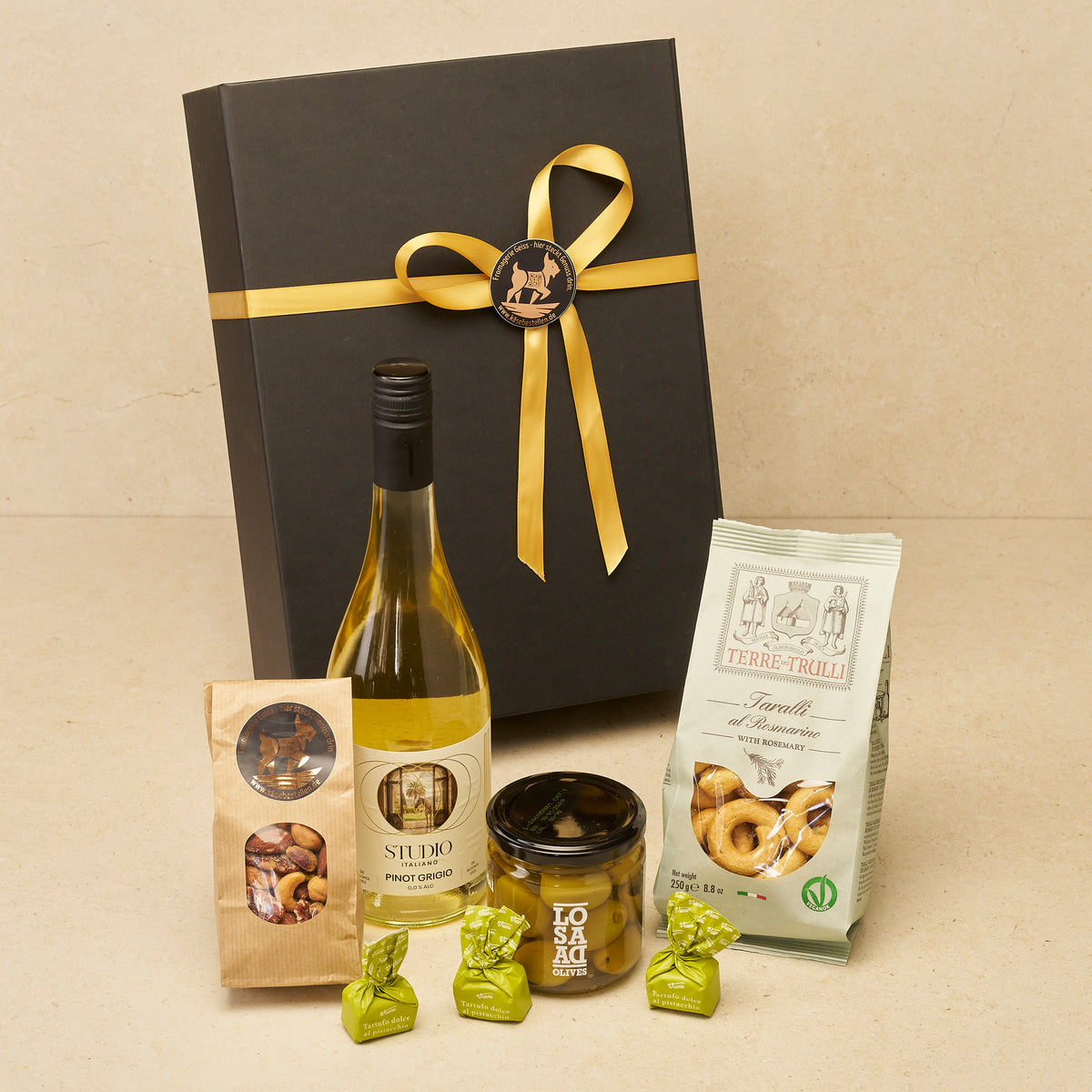 Geschenkbox Weingruß groß alkoholfrei: Pinot Grigio „Studio Italiano“, Nussmix, Tartufi Pistacchio, Gordal-Oliven und Taralli vor der schwarzen Magnetbox