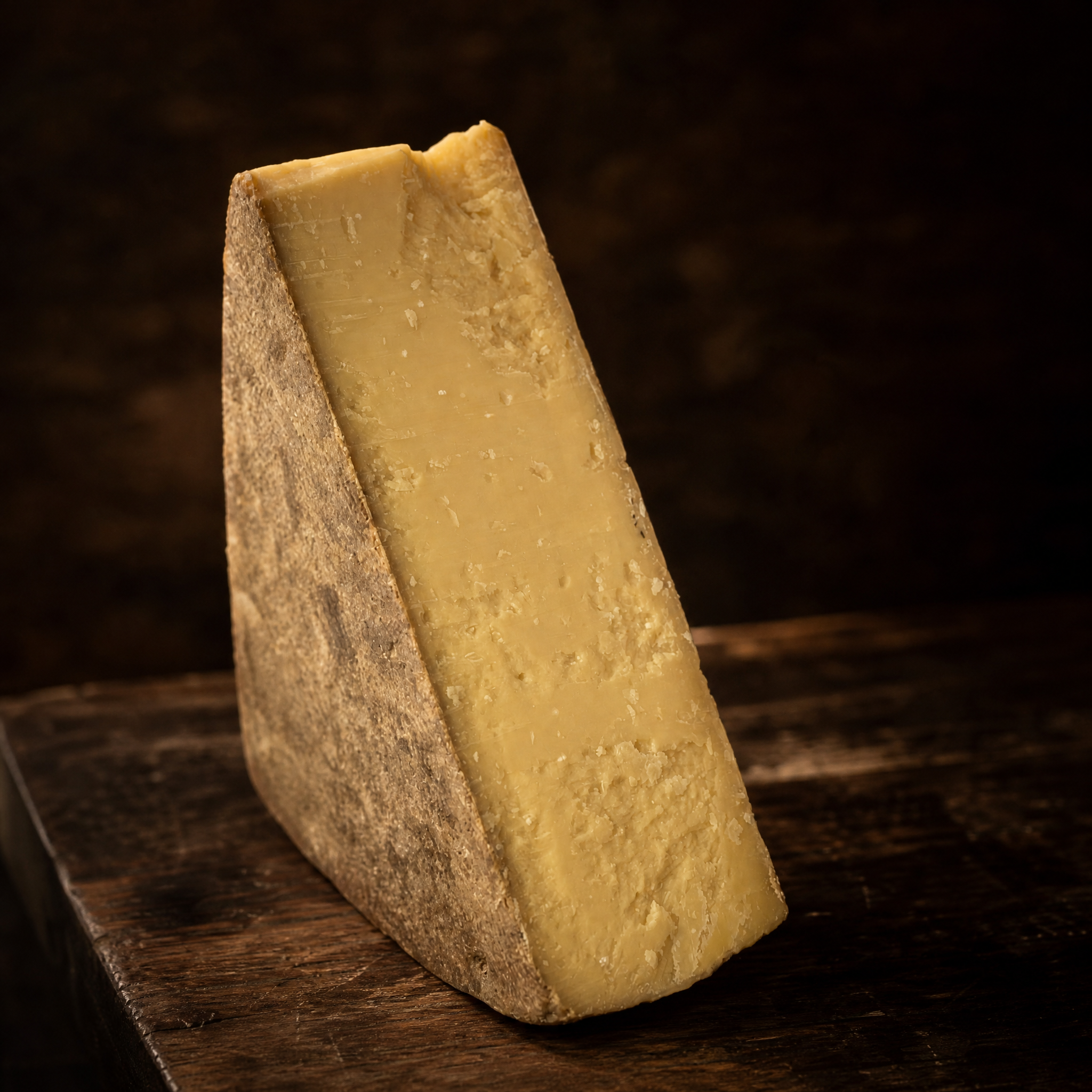 Gruyère Sélection 26M – lang gereifter Hartkäse-Keil mit kristalliner Struktur auf dunklem Holzbrett