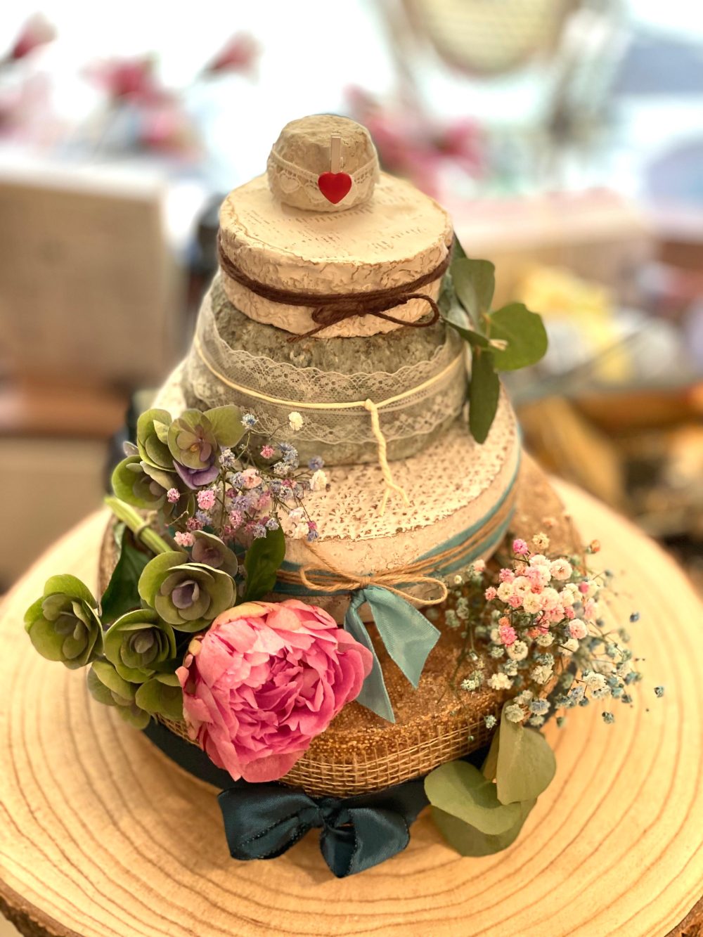 Käsetorte mit rosa Pfingstrose und Eukalyptus auf einer Holzscheibe, Herz-Topper aus Holz