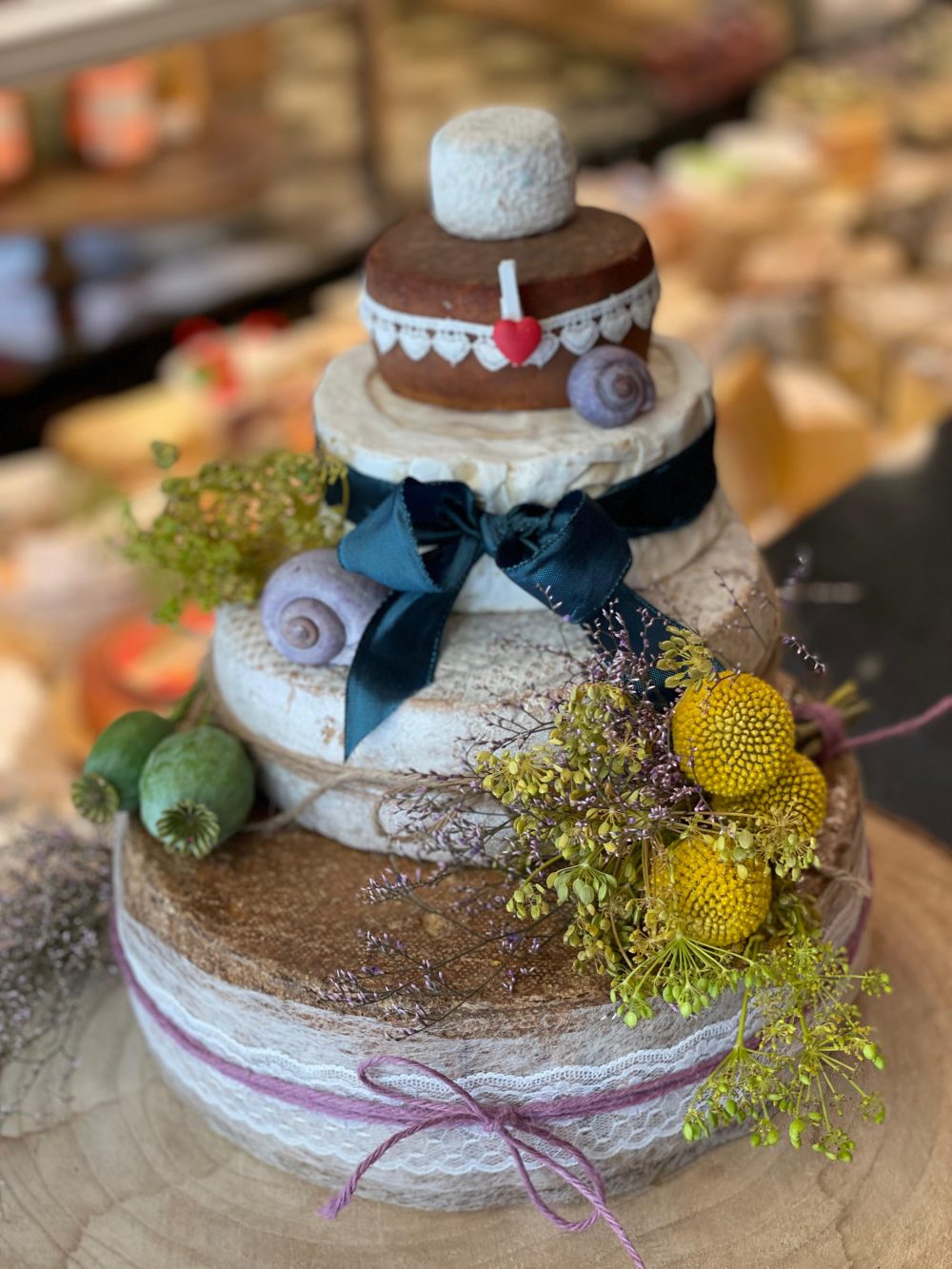 Käsetorte mit petrolfarbener Samtschleife, gelben Craspedia und Spitzenband