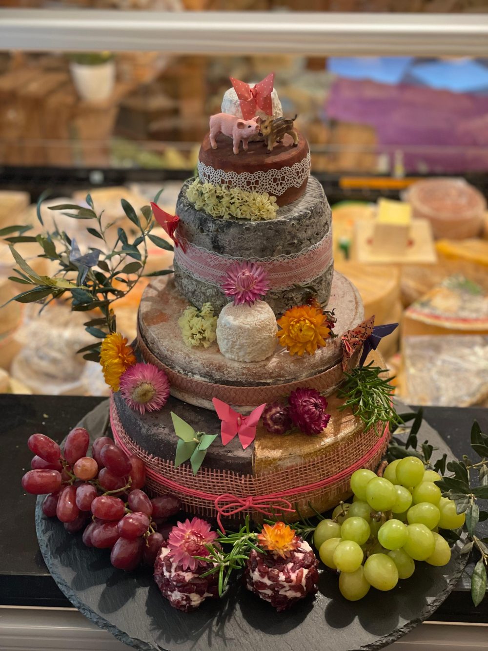 Bunte Käsetorte mit Kranz aus roten und grünen Trauben und Strohblumen in den Etagenfugen