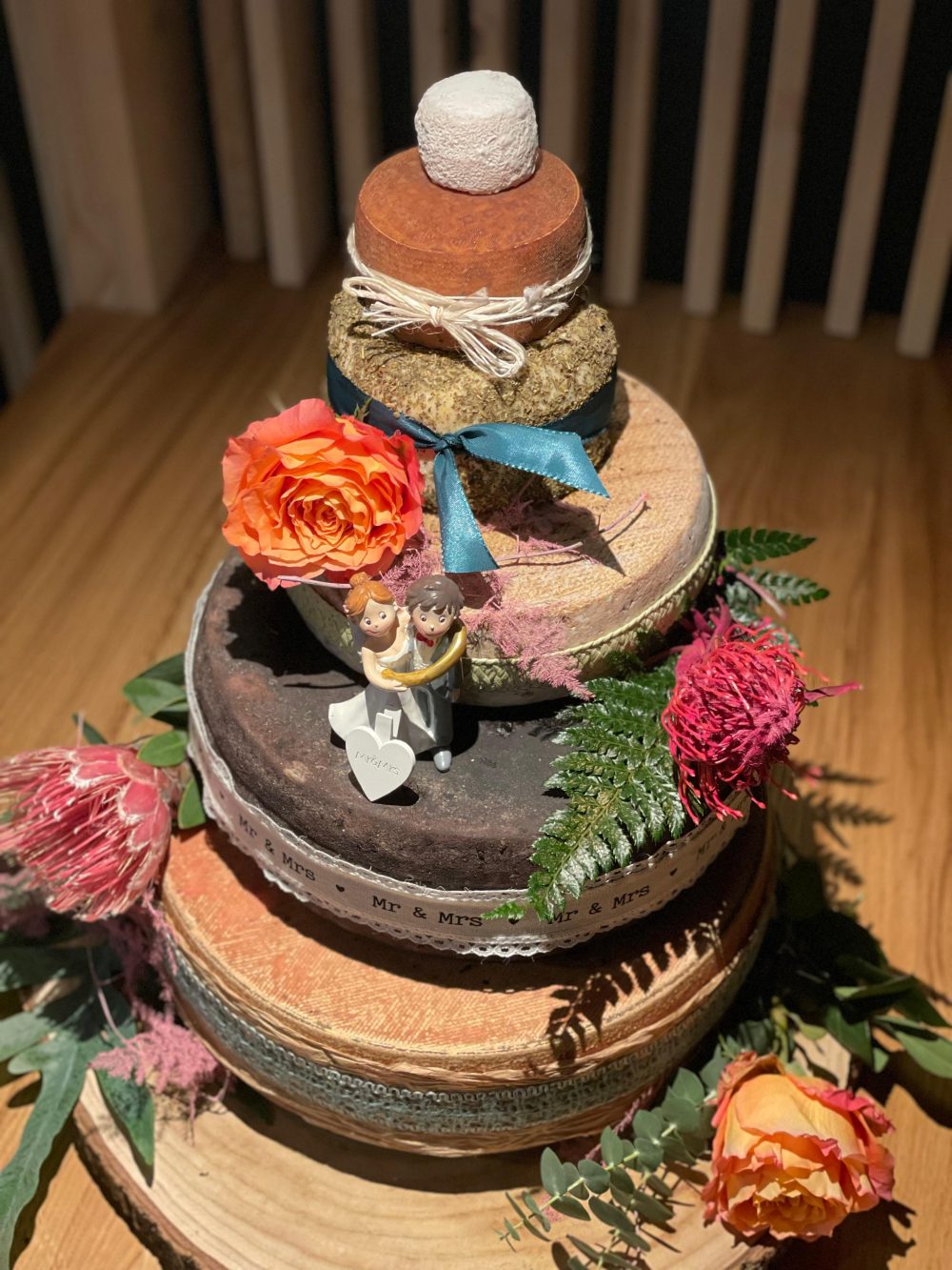 Käsetorte mit orangefarbenen Rosen, Farn und kleiner Brautpaarfigur