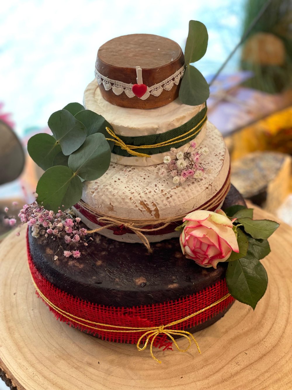 Käsetorte mit rotem Band an der Basis und einer einzelnen Rose als Akzent