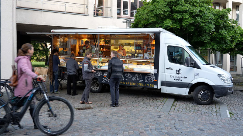 Marktwagen der Fromagerie Geiß mit geöffneter Theke und wartenden Kundinnen