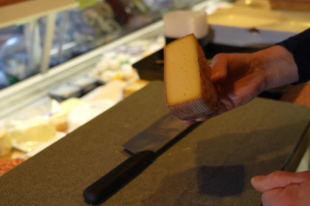 Ein Stück Hartkäse wird am Marktstand auf das Schneidebrett gelegt