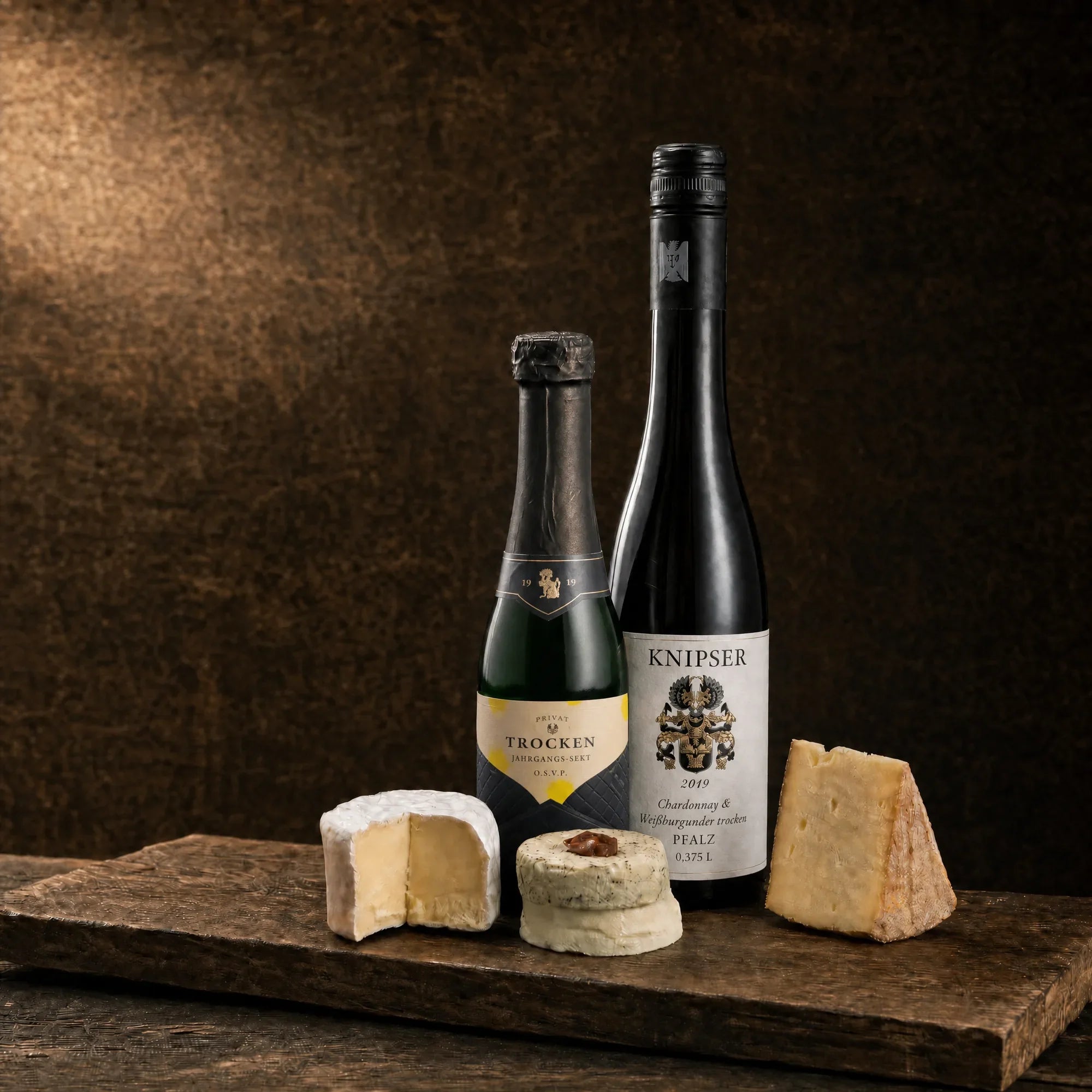 Tasting-Box Duo Élégance: Jahrgangs-Sekt-Piccolo und Weißwein Knipser Chardonnay & Weißburgunder mit Käseauswahl auf rustikalem Holzbrett