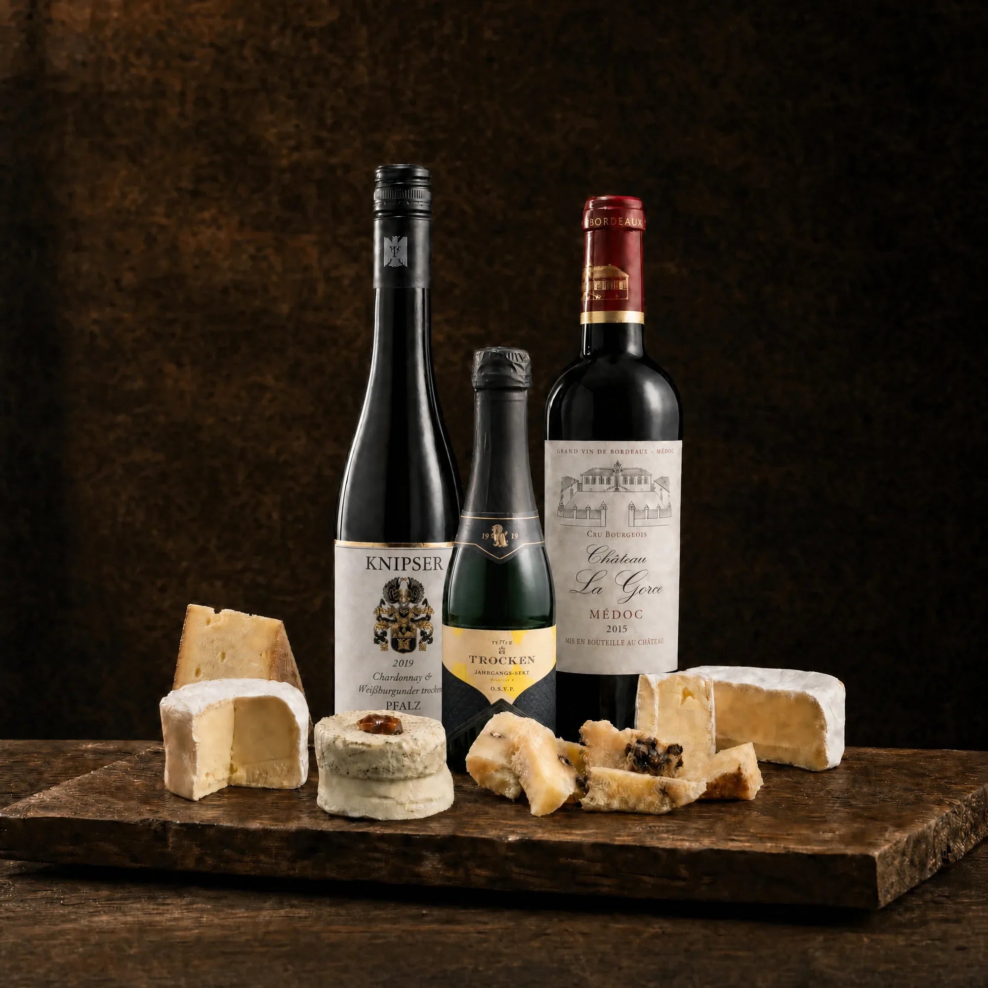 Tasting-Box Trio Royal: Weißwein, Jahrgangs-Sekt-Piccolo und Rotwein Château La Gorce Médoc mit Käseauswahl auf rustikalem Holzbrett